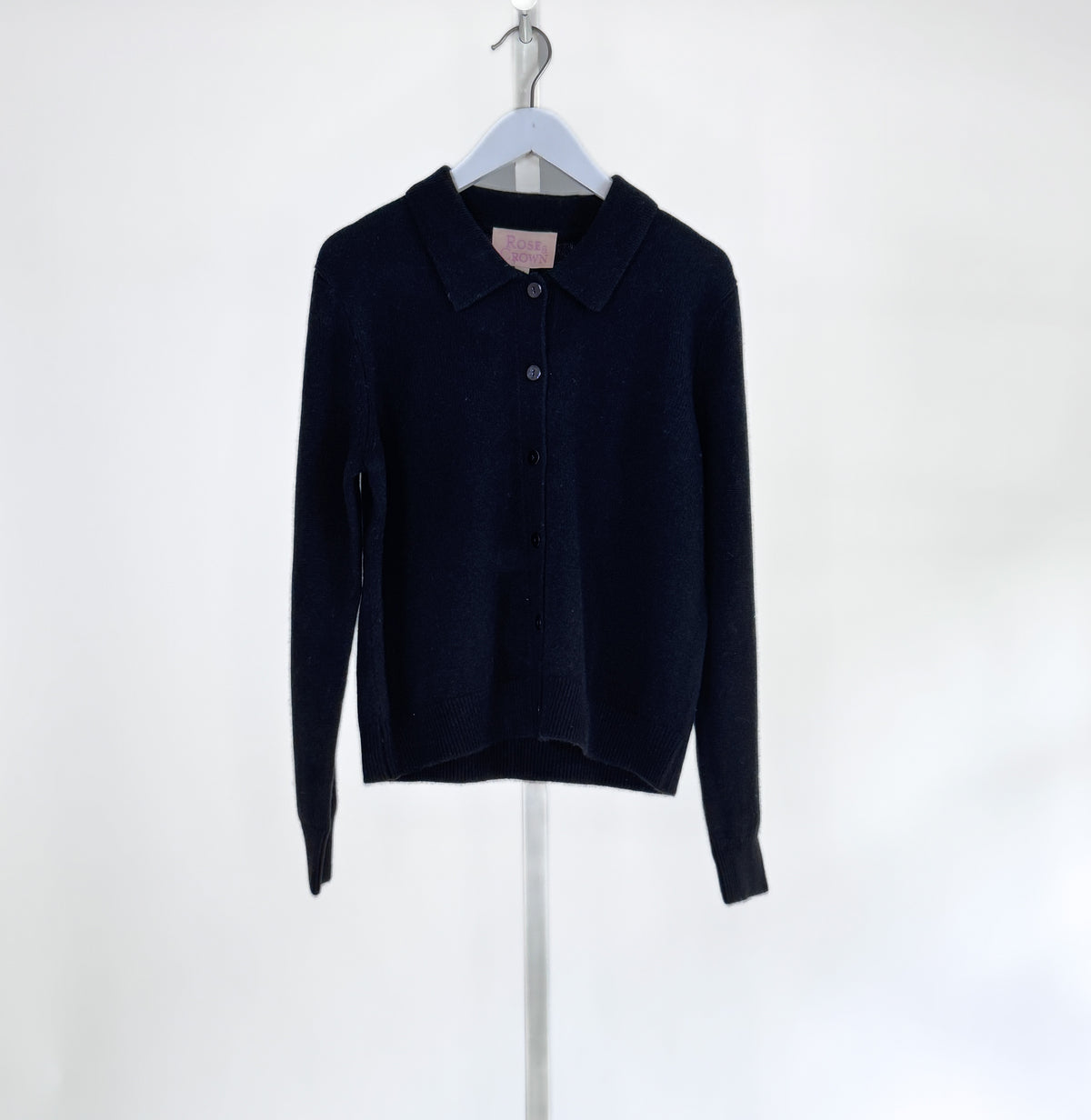 The ROSE &amp; CROWN - CASHMERE CARDIGAN, a luxury long-sleeve button-up in custom-dyed magenta, hangs on a white hanger against a light gray background.