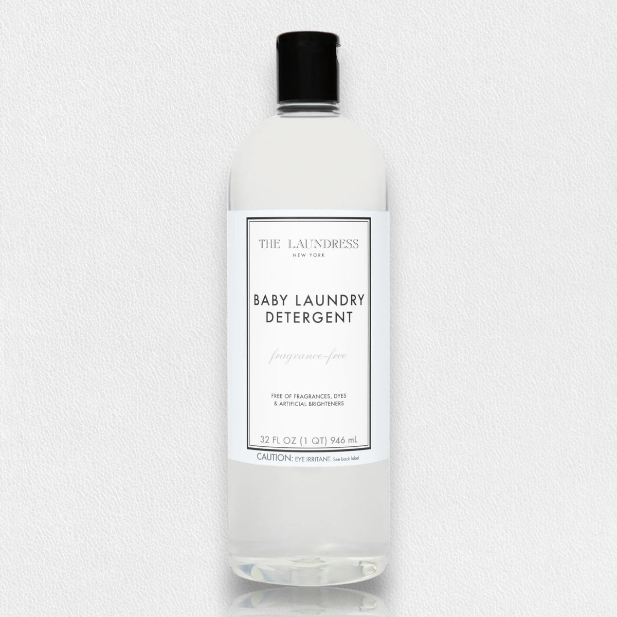 A clear bottle of THE LAUNDRESS - BABY LAUNDRY DETERGENT FRAGRANCE FREE 32OZ, with a black cap. The label indicates it is a pediatrician-tested formula, free of dyes and artificial brighteners. This fragrance-free baby laundry detergent, from THE LAUNDRESS brand, has a volume of 32 fl oz (946 ml). The background is white.