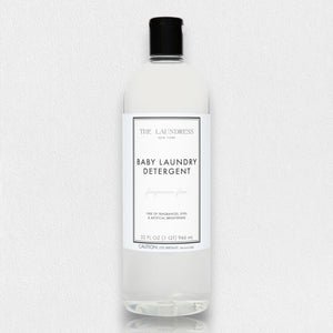 A clear bottle of THE LAUNDRESS - BABY LAUNDRY DETERGENT FRAGRANCE FREE 32OZ, with a black cap. The label indicates it is a pediatrician-tested formula, free of dyes and artificial brighteners. This fragrance-free baby laundry detergent, from THE LAUNDRESS brand, has a volume of 32 fl oz (946 ml). The background is white.