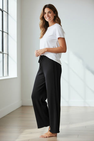 The FRANK & EILEEN BELLA Italian Sweatpant in black features a drawstring waist, side seam detail, and a lightly frayed hem, shown flat on a light textured background.