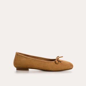 The REQINS - HARMONY SUEDE BALLERINA FLATS IN CAMEL feature a tan suede finish, a small bow on the toe, a low heel, and an elegant, simple design against a plain light background.