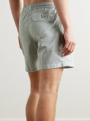 A person wearing HARTFORD - SEERSUCKER SWIM TRUNKS IN GREEN with an elastic waistband and drawstring stands against a plain light background.