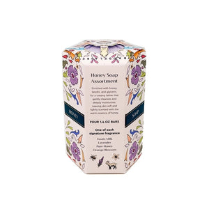 Four pastel-colored, triple-milled soaps—lavender, pink, white, and orange—are stacked next to a decorative floral-patterned box labeled “BAUDELAIRE - HONEY SOAP ASSORTMENT 1.4 OZ QUARTET” by BAUDELAIRE.