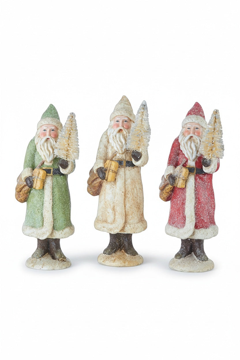 GLITTERED BELLSNICKEL SANTA 8.5″ figurines in green, cream, and red, each holding a small bottle brush tree and a gift; sold individually in assorted colors.