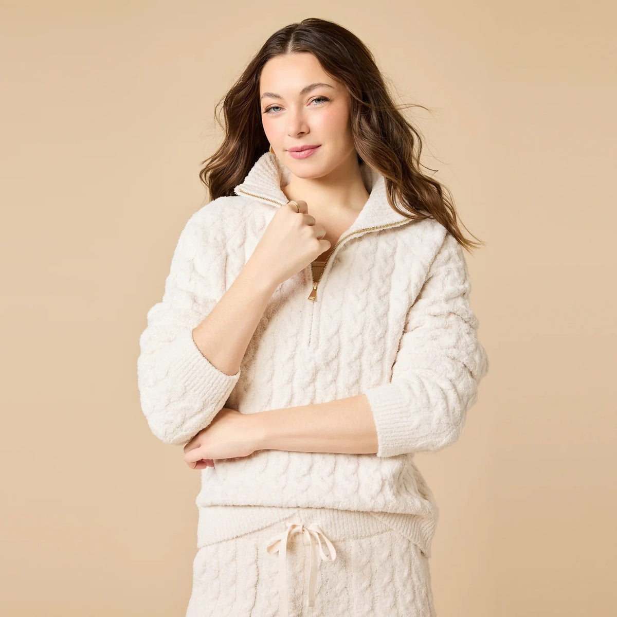 A woman wearing a marshmallow-soft, cream-colored SOFTIES - CABLE KNIT MARSHMALLOW ½ ZIP WITH TAPERED PANT SET, featuring a half-zip pullover and matching pants with a drawstring waist.
