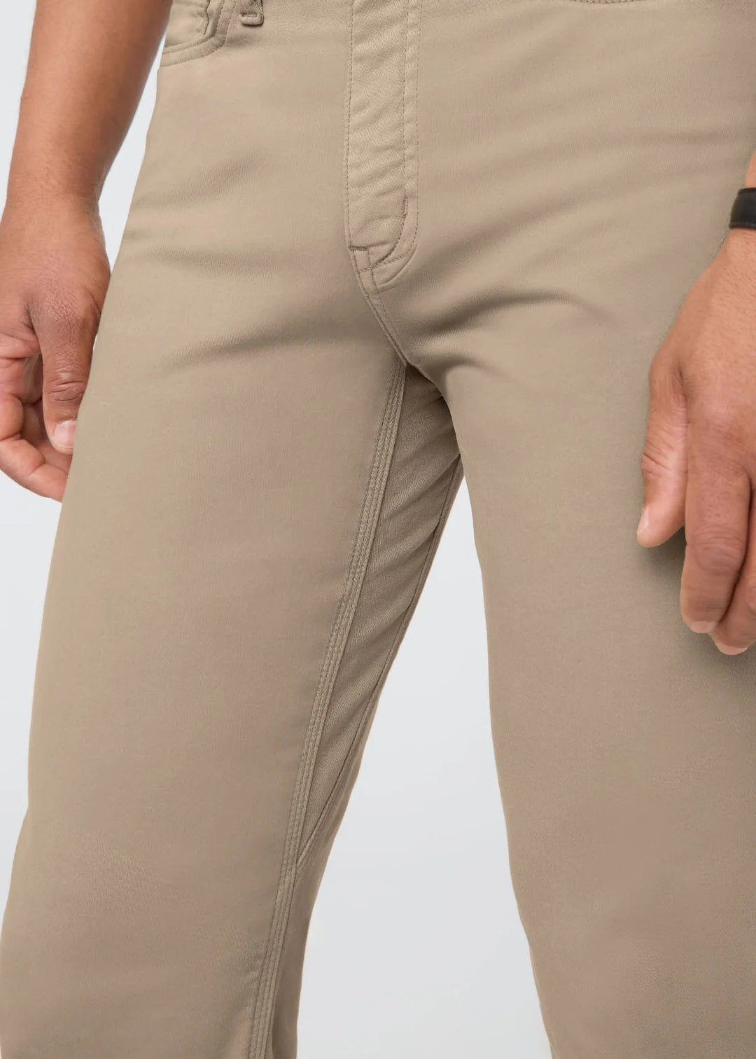 A man with short dark hair stands against a white background, wearing DUER No Sweat Straight Pants in Desert Khaki, a white t-shirt, and white sneakers. He faces the camera with a neutral expression.