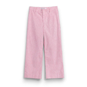 A barefoot person stands on sandy ground near green bushes, wearing FRANK & EILEEN's Wexford Wide Leg Linen Pant in Red Stripe and a white t-shirt, photographed from behind on a sunny day.