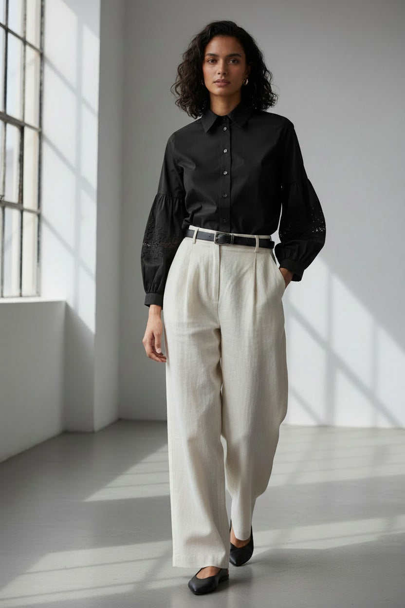 A woman wearing the MILVA MI cotton blouse with embroidered sleeves in black by MILVA, paired with a matching black skirt, poses against a dark gray background.
