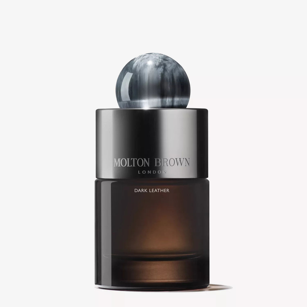 A 100ml bottle of MOLTON BROWN - DARK LEATHER EAU DE PARFUM, with a smoky glass design, metallic cap, and marbled sphere topper from MOLTON BROWN, displayed against a white background.