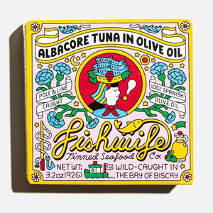A vibrant tin of FISHWIFE Albacore Tuna in Olive Oil features a vintage-inspired design with a woman, flowers, lemons, and banners highlighting the product’s wild-caught and MSC-certified albacore tuna packed in Spanish olive oil.