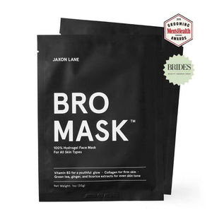 A shirtless man with curly dark hair, a beard, and a chest tattoo lounges outdoors in the sunlight, wearing JAXON LANE's Bro Mask Hydrogel Face Sheet Mask. He holds a drink and relaxes amid greenery, enjoying men's skincare by JAXON LANE.