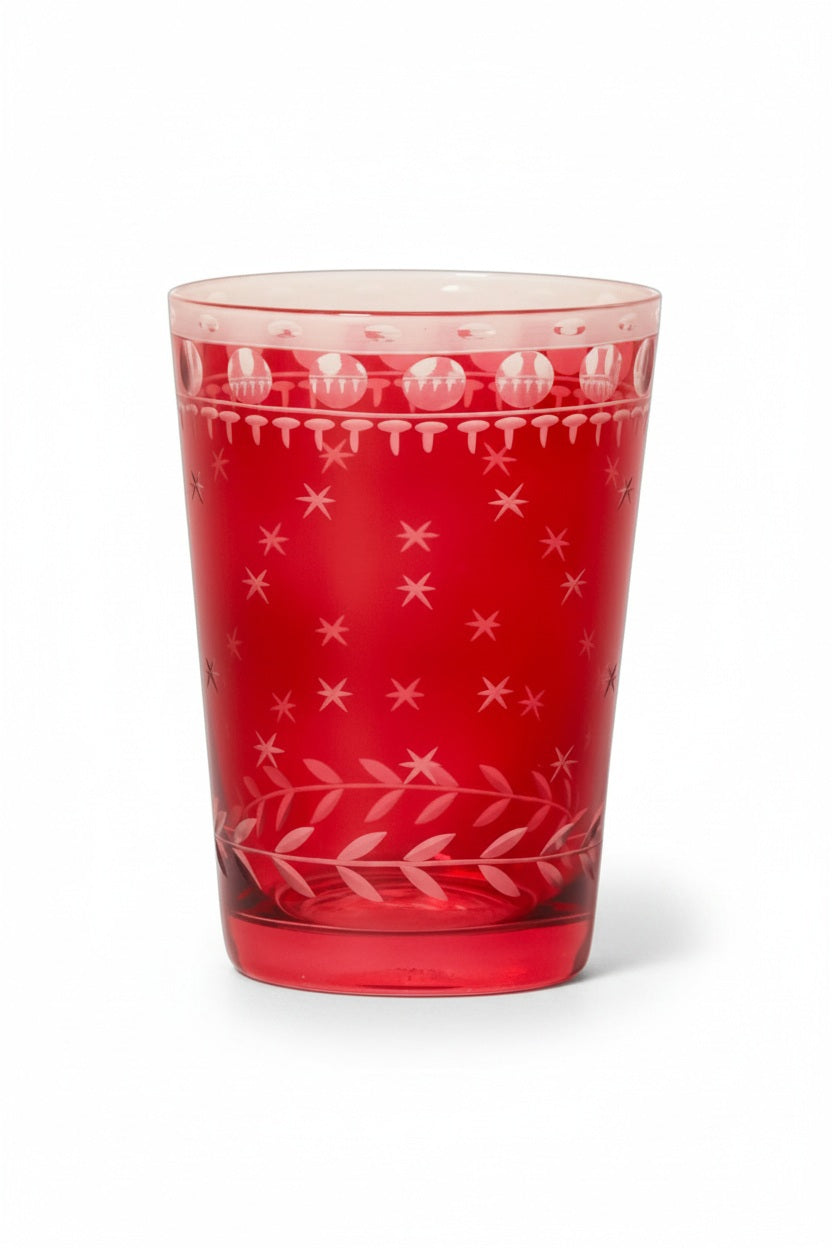 A ZODAX HAND CUT TEA LIGHT CUP, a red borosilicate glass votive holder with etched star and circle patterns, containing a lit candle and sitting on a gold-toned coaster.