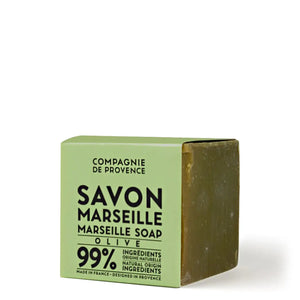 Two cubes of COMPAGNIE DE PROVENCE AUTHENTIC CUBE OF SOAP OLIVE OIL 13.8OZ by CIE LUXE BRANDS, one beige and one olive green, are stacked on a marble sink beside a chrome faucet. Each is labeled “Extra Pur 72% d’Huile.”.