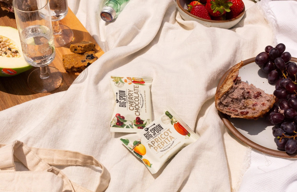 The BIG SPOON ROASTERS - CHERRY CHOCOLATE PEANUT SNACK BAR features a white wrapper with illustrations of cherries, organic dark chocolate cocoa pods, and leaves, plus product details and nut butter ingredient highlights on the front.