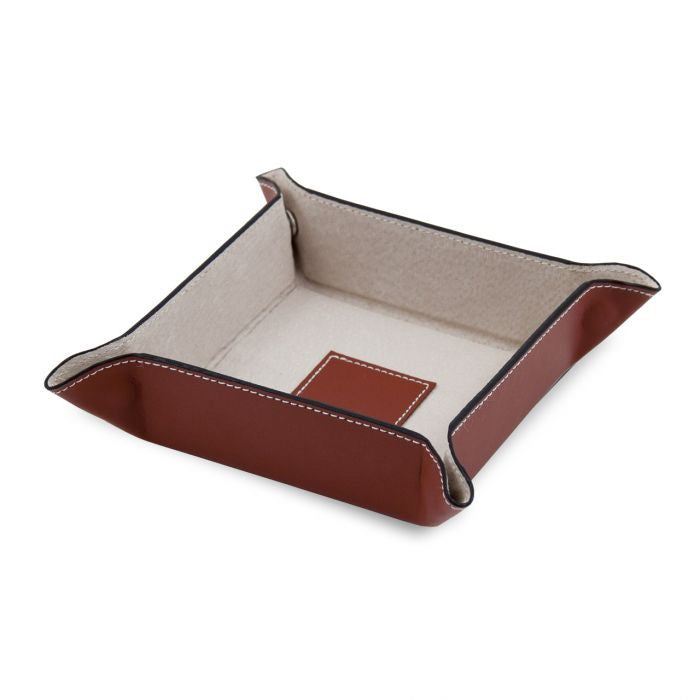 The LEATHER VALET IN SADDLE BROWN by BEYBERK INTERNATIONAL is a square tray with raised edges, visible stitching, and beige pigskin leather lining. A small brown patch accents the center for added detail.
