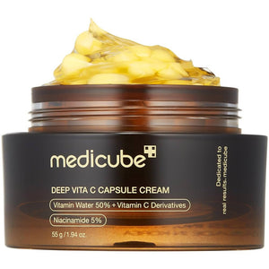 The GLOWISS MEDICUBE DEEP VITA C CAPSULE CREAM, shown in an open jar with yellow capsules on a yellow background and surrounded by lemons, features sea buckthorn, niacinamide, and ascorbic acid to brighten and even skin tone.