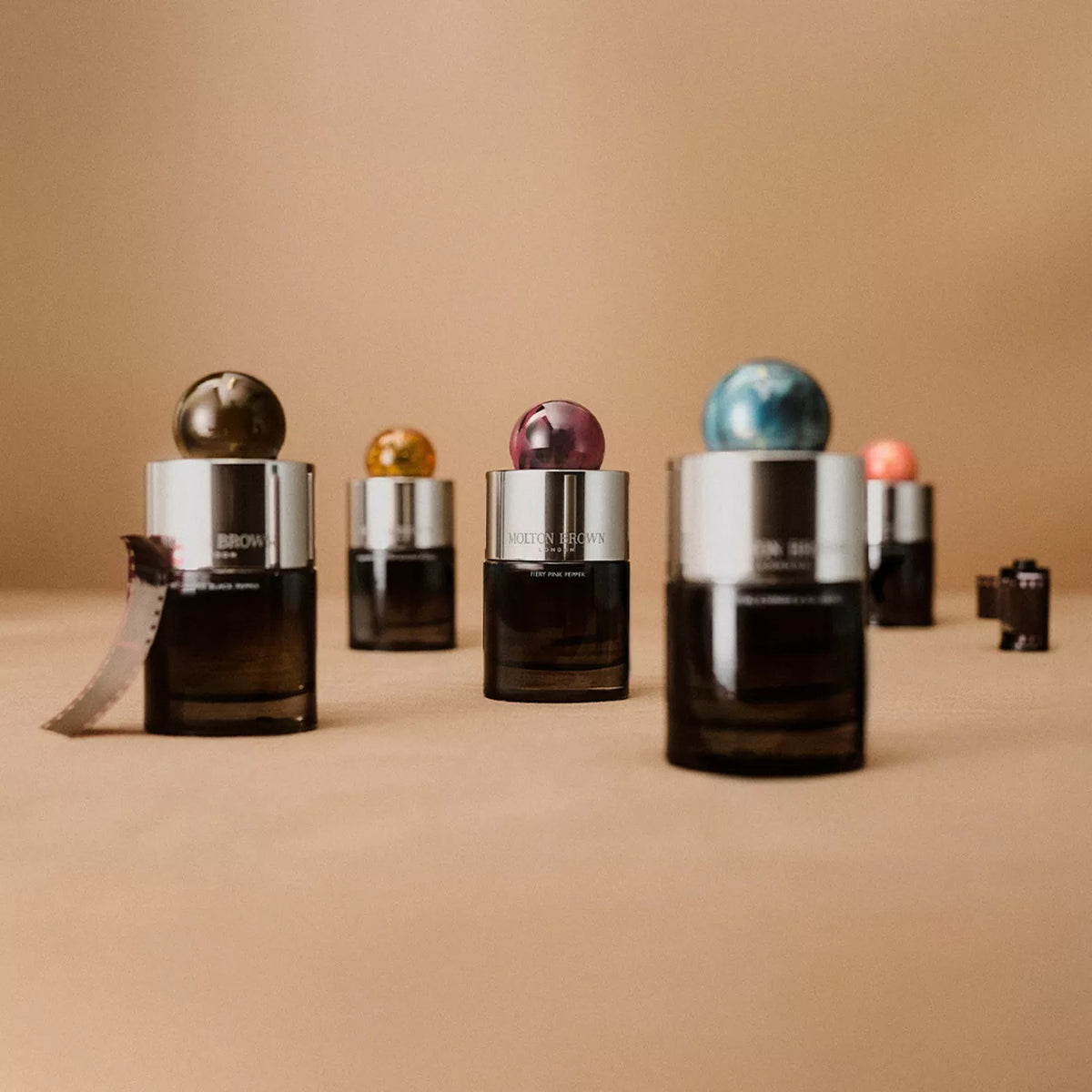 A bottle of MOLTON BROWN - RHUBARB &amp; ROSE EAU DE PARFUM, featuring a matte black body and a round marbled pink cap, displayed against a plain white background.