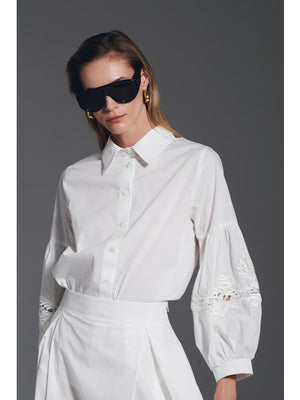 A woman wearing the MILVA MI cotton blouse with embroidered sleeves in black by MILVA, paired with a matching black skirt, poses against a dark gray background.