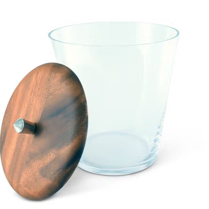 A VAGABOND HOUSE TRIBECA GLASS ICE BUCKET is displayed with an open top beside a round teak lid featuring a small handle. The Mid-Century Modern appeal of its glass and wood textures is elegantly showcased against a white background.