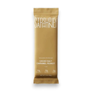 A gold protein bar wrapper labeled “STARS+HONEY” featuring the flavor “Cacao Salt Caramel Peanut” is placed on a beige background, highlighting 10g collagen, 15g protein, and just 2g sugar as a low sugar protein bar option.