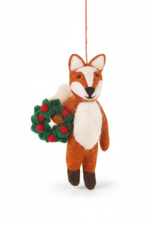 FINLEY FESTIVE FOX ORNAMENT, a handmade felt fox holding a small green wreath with red berries, standing in the snow.