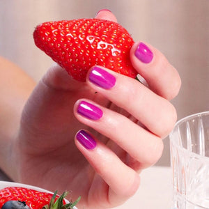 A close-up of MANUCURIST - GREEN™ NAIL POLISH IN ARMERIA by MANUCURIST INC being spread with a brush on a smooth surface, showcasing its vibrant pinky mauve shade, glossy texture, and distinctive curved brushstroke.