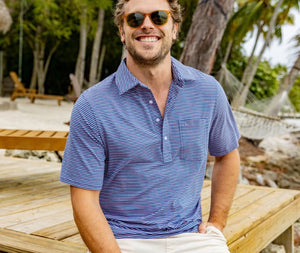 Close-up of a person wearing the CRIQUET Top-Shelf Players Shirt in Stewart Stripe Navy, featuring blue and white stripes, a collar, three buttons, and a small chest pocket. The face is not visible.