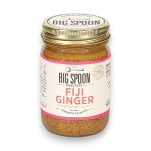 A jar of BIG SPOON ROASTERS - FIJI GINGER ALMOND, featuring a gold lid and a white label with pink accents that displays the brand name, flavor, and additional product information. The crystallized ginger-infused almond butter is visible through the clear jar.