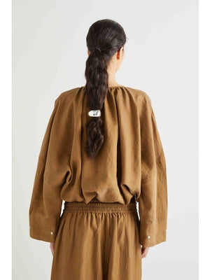 A woman with long dark hair tied back wears the MEIMEIJ Cotton Bomber Jacket—loose-fitting and lightweight—in brown, paired with matching high-waisted pants. She stands against a plain light background.