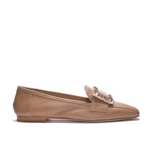 A side view of the MICHELE LOPRIORE - MARZIA LOAFER in genuine beige leather with a flat heel. The shoe features a pointed toe and an ornate gold-toned rectangular buckle adorned with small crystal accessories on the upper part. Made in Italy by MICHELE LOPRIORE, it sits against a plain white background.