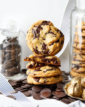 A white pouch of MAISON ZOE FORD BILLIONAIRE CHOCOLATE CHIP COOKIE Mix, showing stacked chocolate cookies with chocolate pieces and baking ingredients, promises an easy, bakery-quality cookie experience from MAISON ZOE FORD.