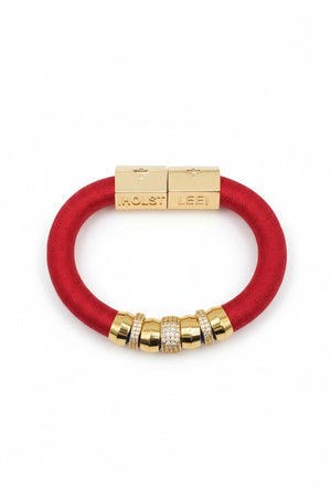 The HOLST + LEE - LUXE CLASSIC BRACELET by HOLST & LEE features an elegant orange cord with gold-plated accents, including a rectangular gold clasp adorned with several gold and diamond-encrusted beads near the clasp.