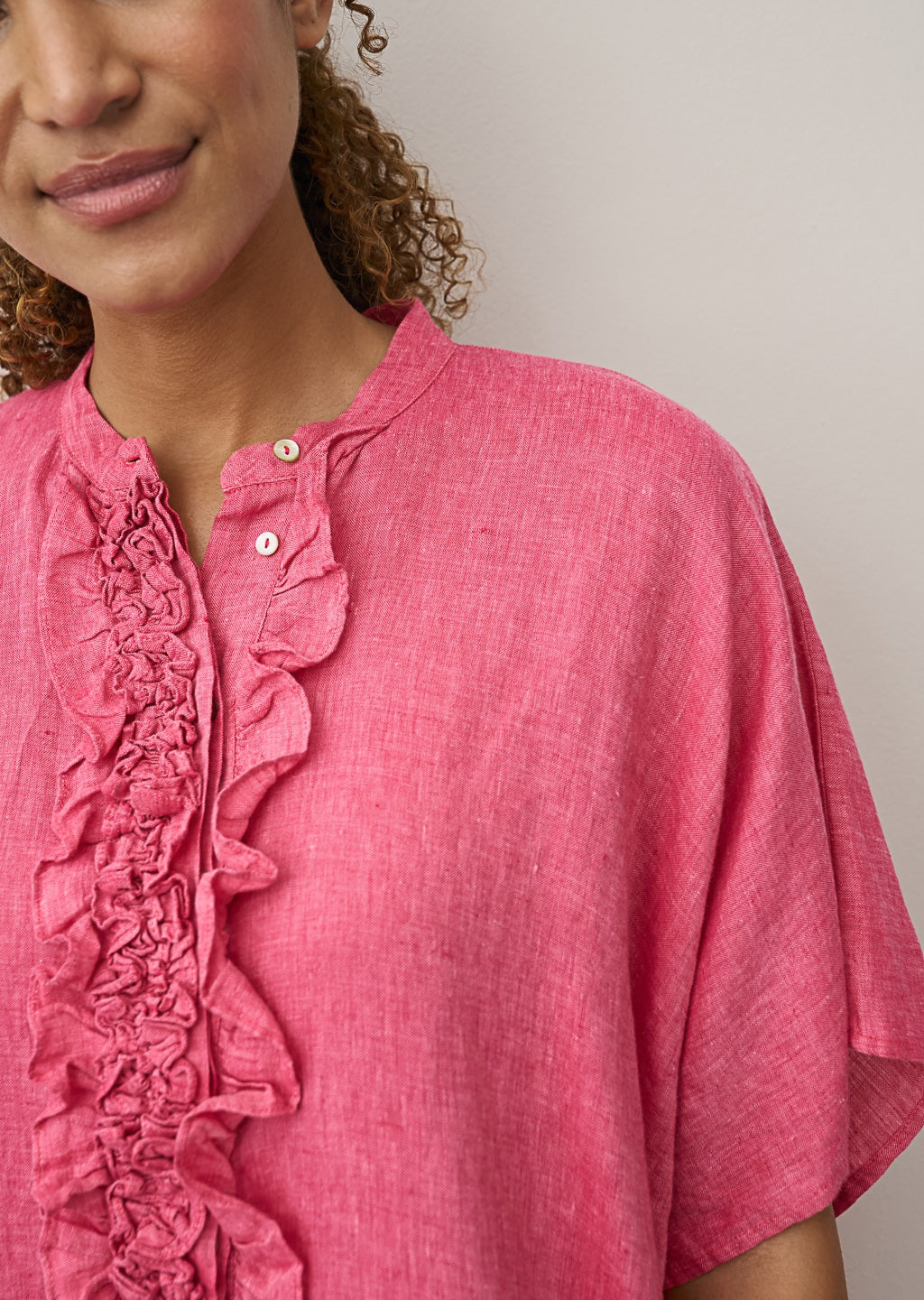 A woman models the 0039 ITALY DAISY LINEN DRESS, featuring ruffled detailing along the button placket. Only her lower face and upper torso are visible as she stands against a light background, showcasing modern femininity.