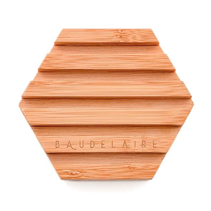 A pink hexagonal soap featuring a honeycomb and pinecone motif, reminiscent of the elegant Baudelaire honey soap, is elegantly displayed on the BAUDELAIRE Bamboo Hex Soap Dish—an eco-friendly wooden accessory by BAUDELAIRE.