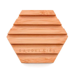 A pink hexagonal soap featuring a honeycomb and pinecone motif, reminiscent of the elegant Baudelaire honey soap, is elegantly displayed on the BAUDELAIRE Bamboo Hex Soap Dish—an eco-friendly wooden accessory by BAUDELAIRE.
