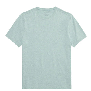 A man with short hair stands with his back to the camera, wearing the MACK WELDON Slub Cotton Crew Neck T-Shirt in Nile Blue Heather and dark pants. His hands are in his pockets as he glances over his left shoulder.