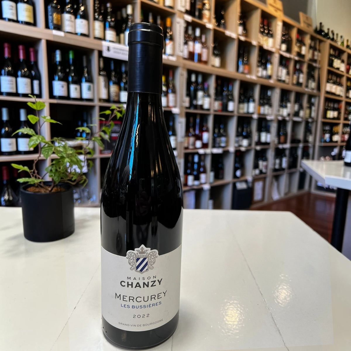 A bottle of MAISON CHANZY ‘LES BUSSIERES’ MERCUREY 2022 with a dark foil capsule and a cream-colored label featuring a blue and white crest.