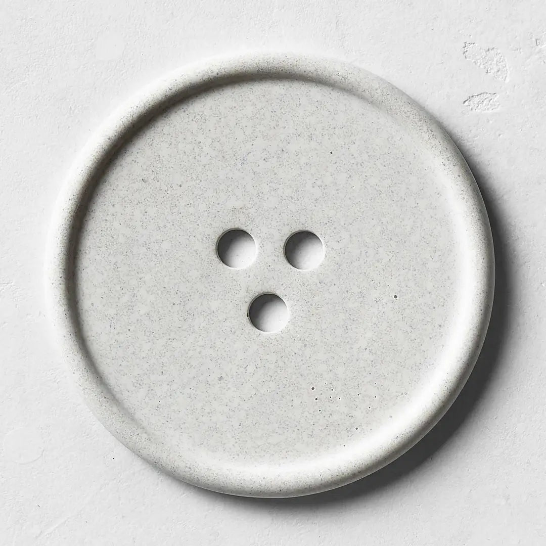 The UME - GREY BOUTON ERODE SOAP DISH by UME STUDIO features a large, round, light gray design inspired by the Bouton series, echoing the look of a minimalist handmade tray or concrete dish.