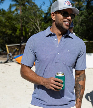 A close-up of a person wearing the CRIQUET - Oxford Pique Players Shirt in First Mate, featuring white buttons, a left chest pocket with a small embroidered logo. The person's face is not visible.