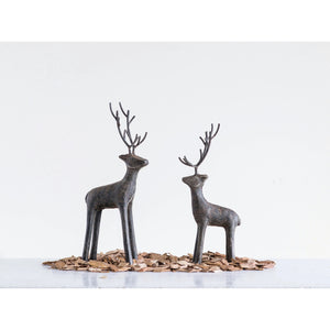 The CREATIVE COOP CAST IRON STANDING DEER features two minimalist black metal sculptures with tall antlers, displayed on wood chips against a white background, adding a striking modern touch to your holiday decor.