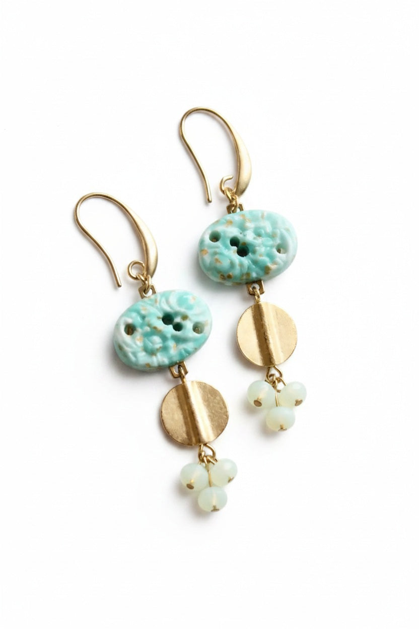 The DAVID AUBREY - VINTAGE TURQUOISE GLASS CLUSTER EARRINGS by DAVID AUBREY feature gold plated ear wires, turquoise glass beads, round gold accents, and delicate clusters of small white beads, beautifully displayed on a round white surface.
