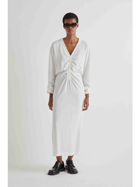 A person with short hair wears the MEIMEIJ Gathered Waist Long Sleeve Dress in Black, styled with dark sunglasses and black chunky shoes, standing against a plain white background.
