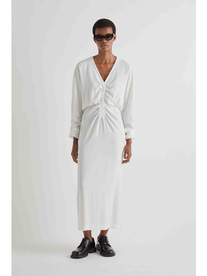 A person with short hair wears the MEIMEIJ Gathered Waist Long Sleeve Dress in Black, styled with dark sunglasses and black chunky shoes, standing against a plain white background.