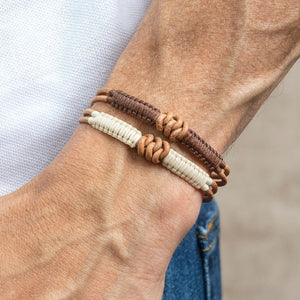 A close-up of a wrist wearing the MAKARLA Men's Knot Leather Bracelet, adjustable in olive green, featuring knotted details. The person is dressed in a white shirt and blue jeans.