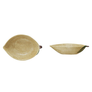 A flat lay features CREATIVE COOP’s HAND-PAINTED STONEWARE LEMON SHAPED BOWL, SMALL—one with oats, one with a grapefruit—plus a lemon-shaped pitcher and ceramic lemons atop a folded striped cloth. A delightful citrus-themed display.