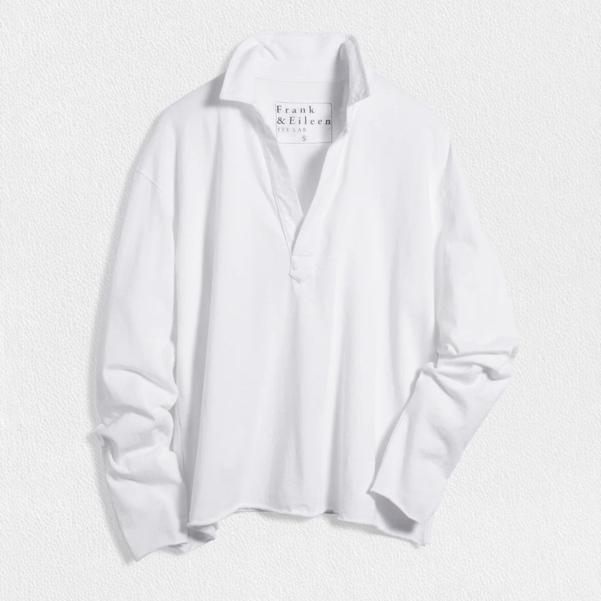 The FRANK &amp; EILEEN Patrick Popover Henley in Heritage Jersey White, a relaxed-fit long-sleeve shirt with an open neckline, is shown laid flat on a textured white surface. The tag displays the FRANK &amp; EILEEN brand name.