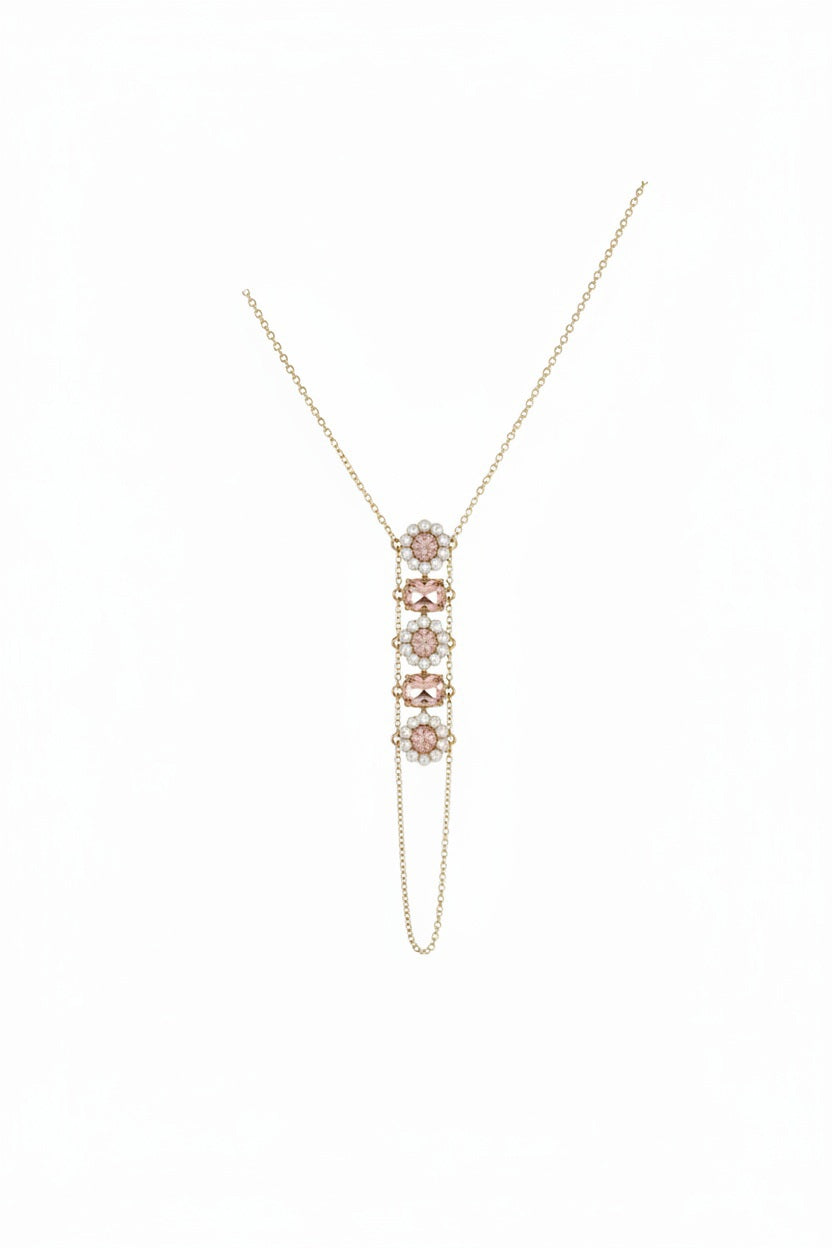 The GOLDISH - FLOWER PINK MOONSTONE AND WHITE PEAR LADDERS TO BLISS NECKLACE by GOLDISH features a vertical floral pendant with four pink moonstones and small clear stones, inspired by sacred geometry. Displayed on a beige fabric bust.