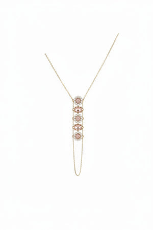 The GOLDISH - FLOWER PINK MOONSTONE AND WHITE PEAR LADDERS TO BLISS NECKLACE by GOLDISH features a vertical floral pendant with four pink moonstones and small clear stones, inspired by sacred geometry. Displayed on a beige fabric bust.