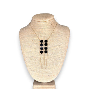 The GOLDISH DOUBLE LADDERS TO BLISS BLACK ONYX CIRCLE STONE NECKLACE, featuring three vertical rows of black onyx stones, is shown on a beige fabric bust stand against a white background.