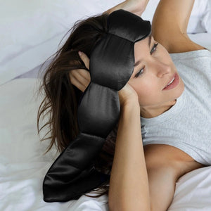 The NODPOD Silk Weighted Sleep Eye Mask in Noir by NODPOD is a dark blue, segmented eye mask featuring a strap-free design and unique four-pad shape. Text highlights its calming effect for stress relief and relaxation, all set against a light background.